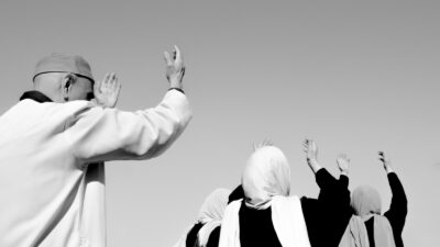 A Muslim man and woman praying with their arms raised to the sky