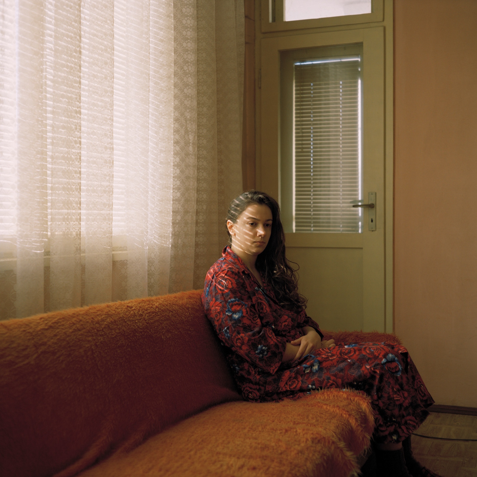 Vera Hadzhiyska self portrait, sitting on a couch in her grandparents' Soviet-style apartment