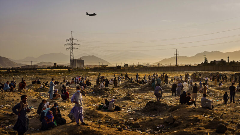 A military transport plane departs overhead as Afghans hoping to leave the country wait outside the Kabul airport on Aug. 23, 2021. Since the Taliban takeover of Afghanistan earlier in August, more than 120,000 people were airlifted out of Afghanistan in one of the largest mass evacuations in U.S. history.