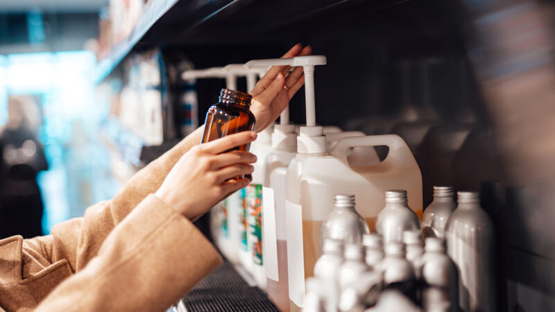 Young woman refilling shower gel / body wash into a reusable glass bottle in zero waste store. Shopping eco friendly personal skincare products. Zero waste concept. Creating a plastic free planet.