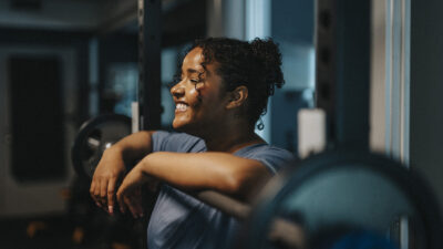 Smiling young woman leaning on barbell at health club