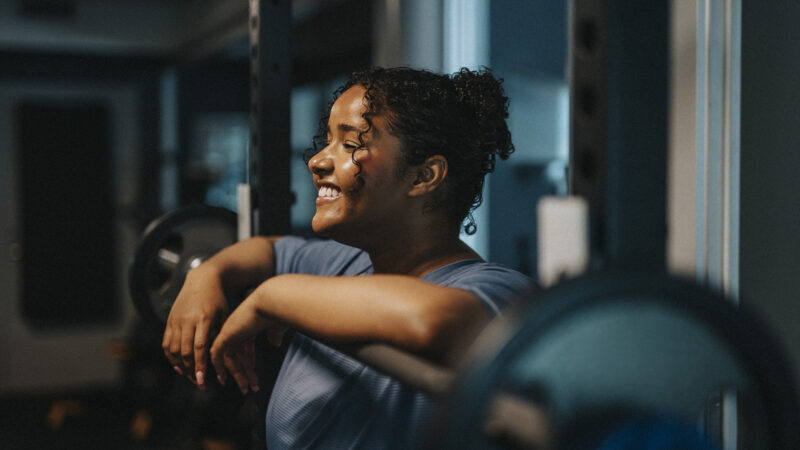 Smiling young woman leaning on barbell at health club