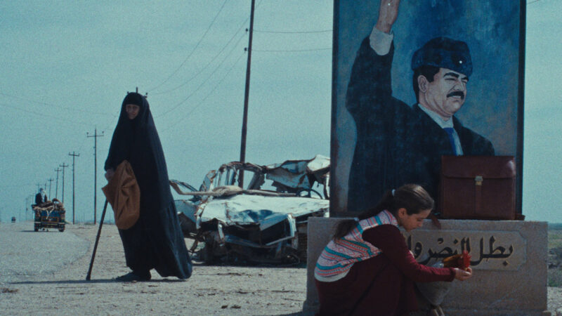 A still from The President's Cake showing a woman in an abaya standing by a road