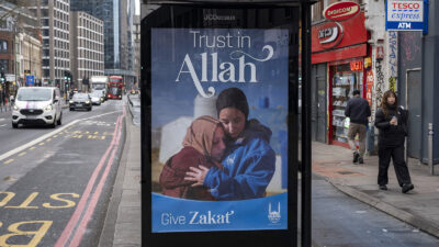 A bus station poster advertising zakat giving shows two Muslim Women embracing and text that reads 'Trust in Allah'.