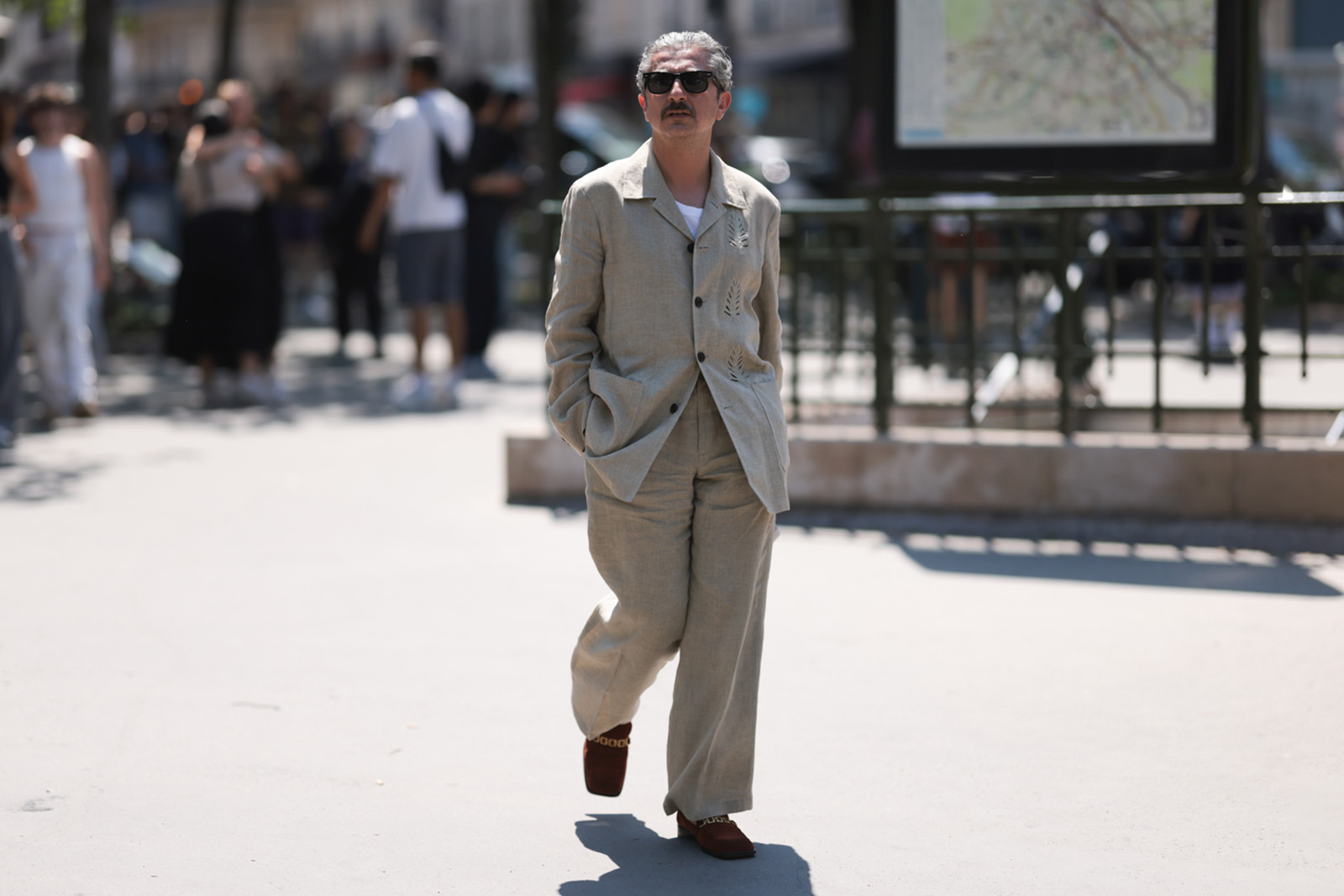 Fashion Week Guest is seen wearing black shades, a white shirt, a beige and brown buttoned linen suit which has three tree stickers on it, with red and golden shoes outside the Sacai Menswear Spring Summer 2024 show as part of Paris Fashion Week on June 25, 2023