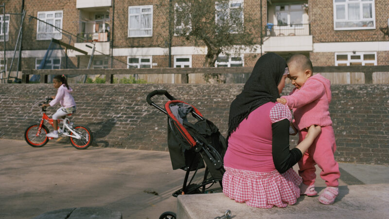 A young mother, who is a recent immigrant, plays with her daughter on the playground of the Kingsmead Estate in Homerton, in the eastern part of Hackney. The estate has 980 flats and houses more than 3,000 people. Built in 1939, it has developed a reputation as a sink estate with a variety of social problems, gangs, vandalism, and crime. In recent years there have been initiatives to regenerate the estate and establish a more coherent sense of community. With its close proximity to the site of the 2012 Olympic Games more resources have become available, however, there are still substantial difficulties. Many residents are recent immigrants or asylum seekers and poverty remains a huge challenge. There are 42 different languages spoken by children at the local Kingsmead Primary School, where 95% of the pupils are from an ethnic minority.
