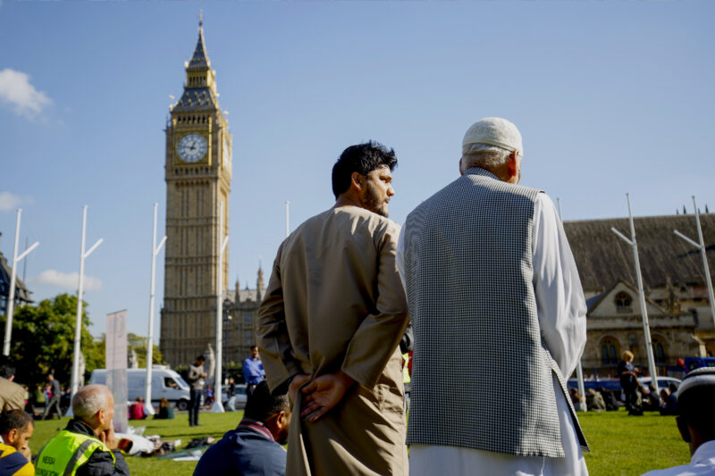 Two men in Muslim dress in the foreground, with Big Ben and Parliament Square visible before them