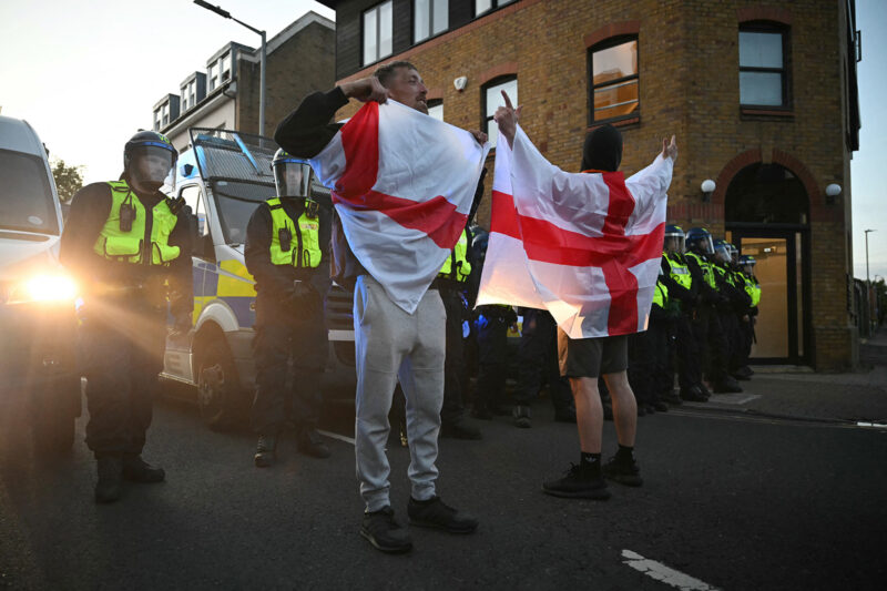 Two people hold aloft St George's cross flags, in front of a line of police