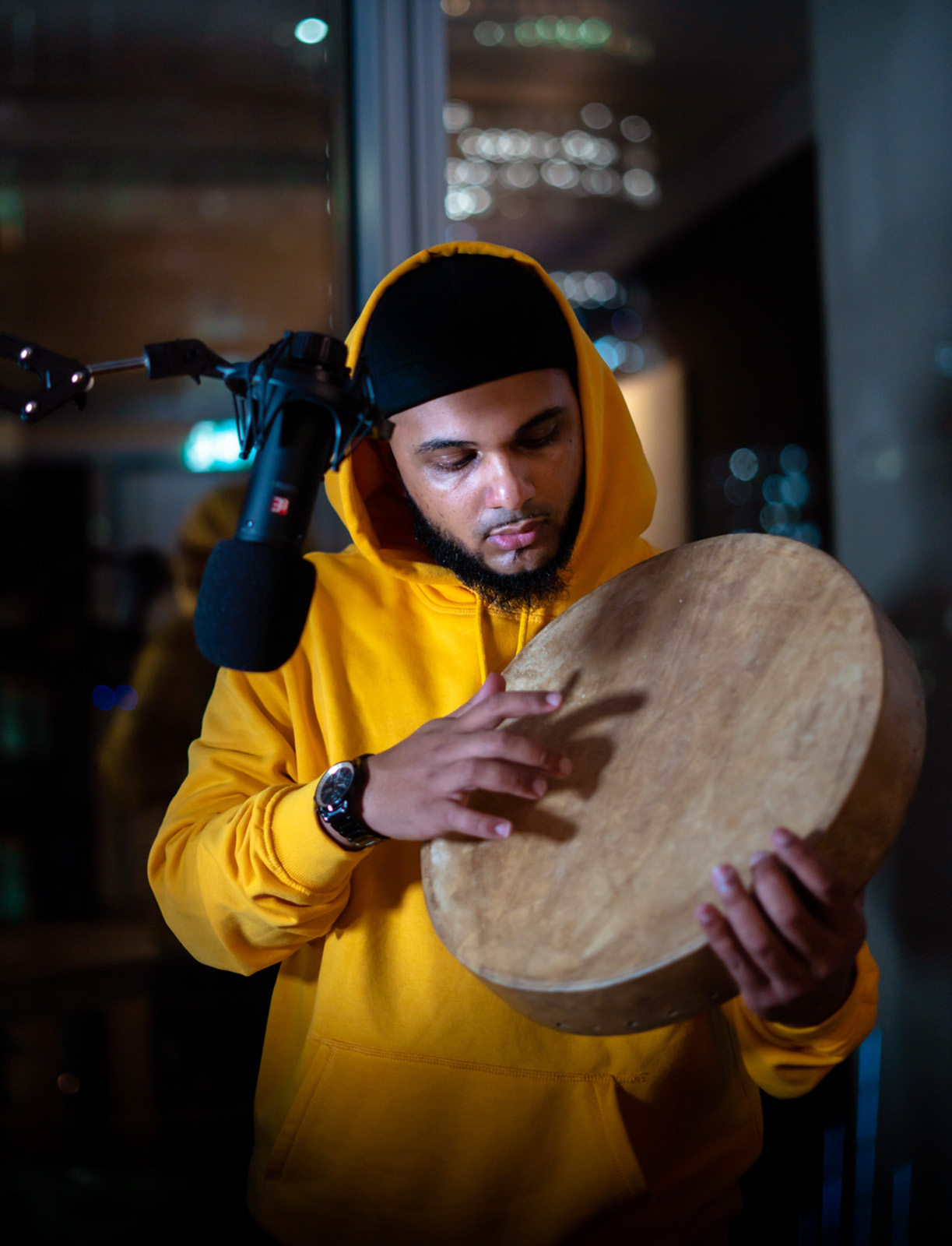 Photograph of Halal Beats/Umar Valu holding a hand drum to a microphone in a recording studio.