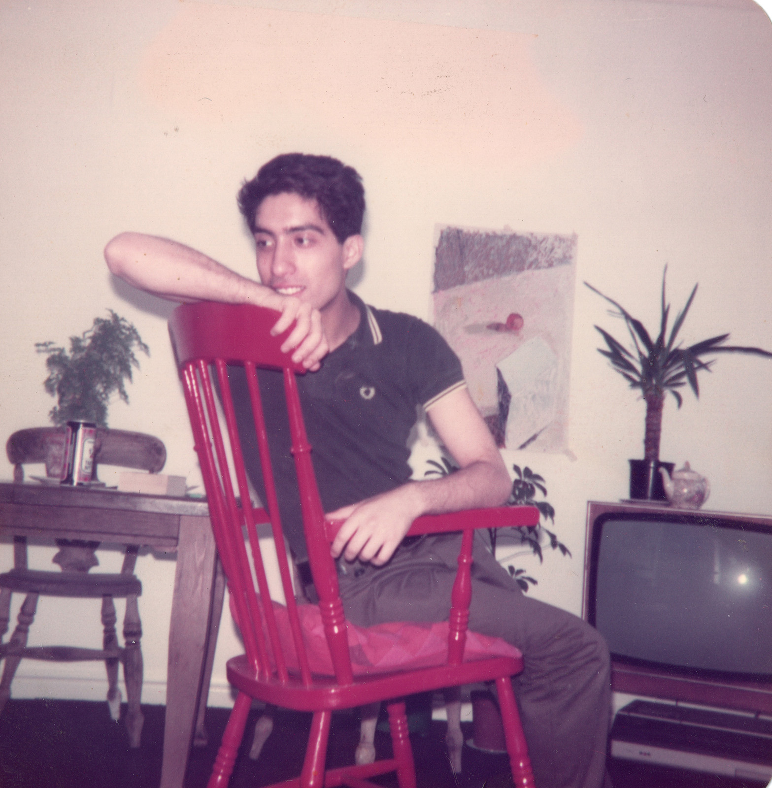 Photograph of Hamad Butt sitting on a red chair in what appears to be a living room. TV in the background. 