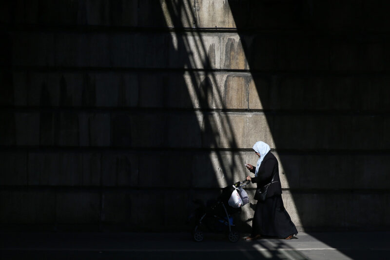 Stock image of a Muslim woman pushing a buggy under a railway bridge in London.