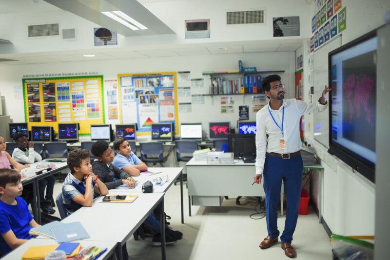 Stock image of male teacher leading lesson at touch screen in classroom