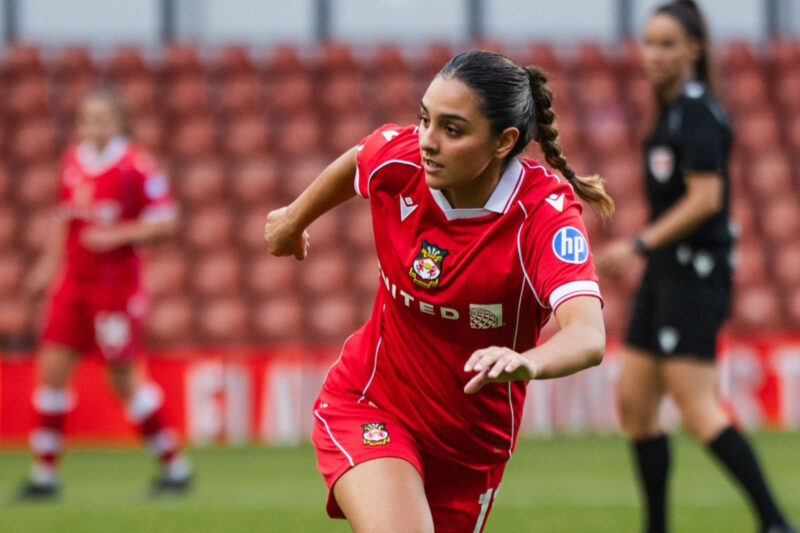 Mariam Mahmood in a red strip, pictured while running towards the camera on a football pitch, looking to one side.