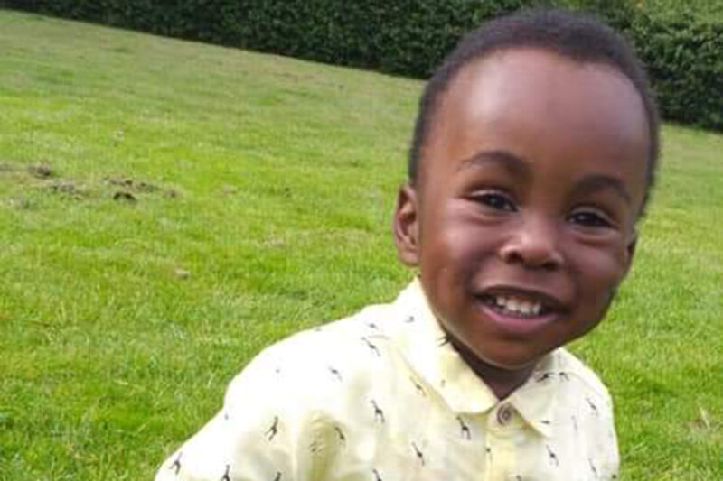 A smiling little boy in a yellow shirt against a background of green grass