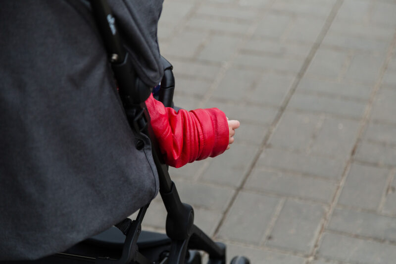 A baby's hand poking out of a red sleeve, visible from behind as it sticks out of a buggy