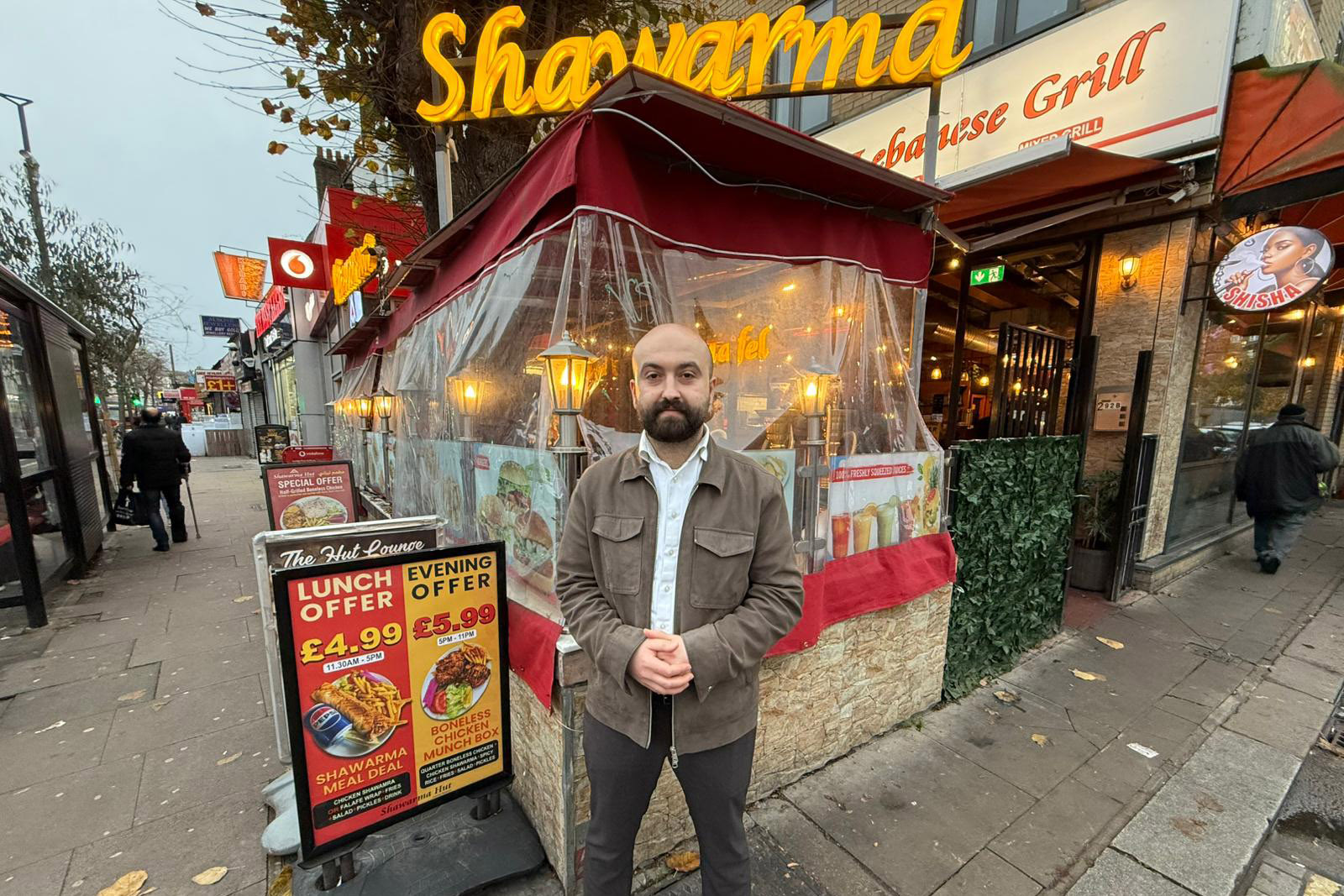 Ali Alsahlane, who wants people to be able to eat out on universal credit, outside his restaurant Shawarma Hut, whose sign is in yellow cursive writing. Ali has his hands folded and looks happy