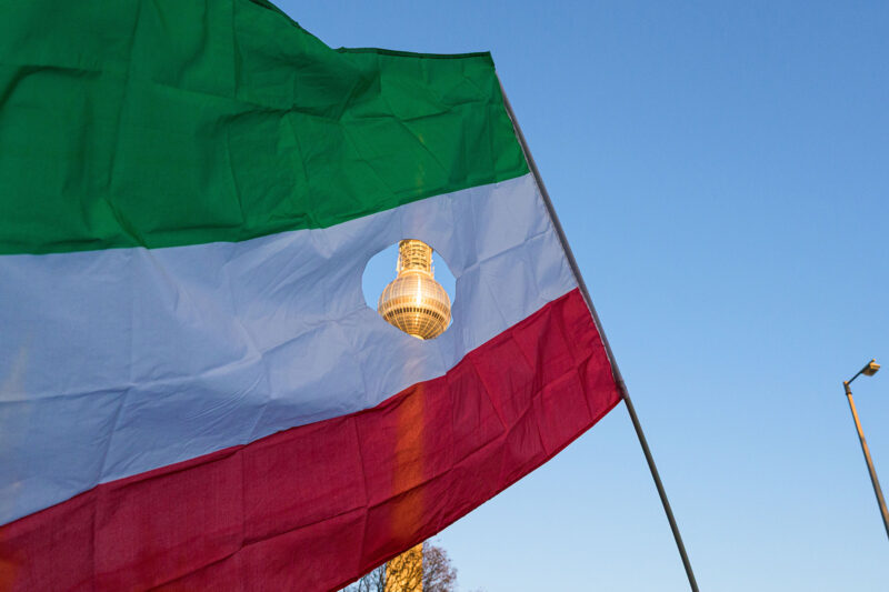 Berlin's TV Tower, visible through a hole in an Iranian flag with the Islamic Republic of Iran symbol cut out, at a protest on Saturday 18 January