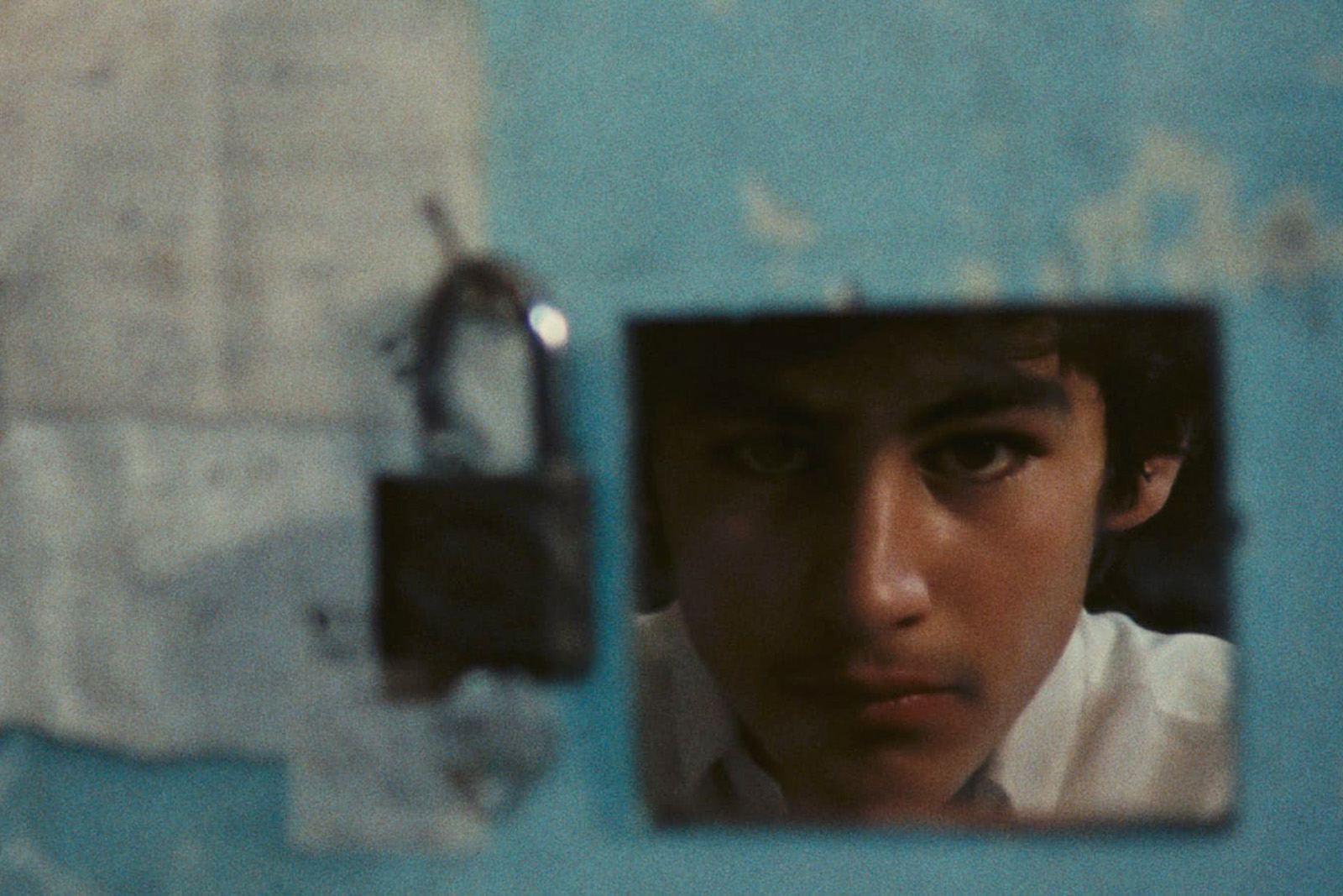 Image taken from a still from A Wedding Suit (1976) directed by Abbas Kiarostami, showing as part of The Barbican's Masterpieces of the Iranian New Wave programming, 2026. Reflection of a boy appears in a square mirror against a backdrop of a wall.