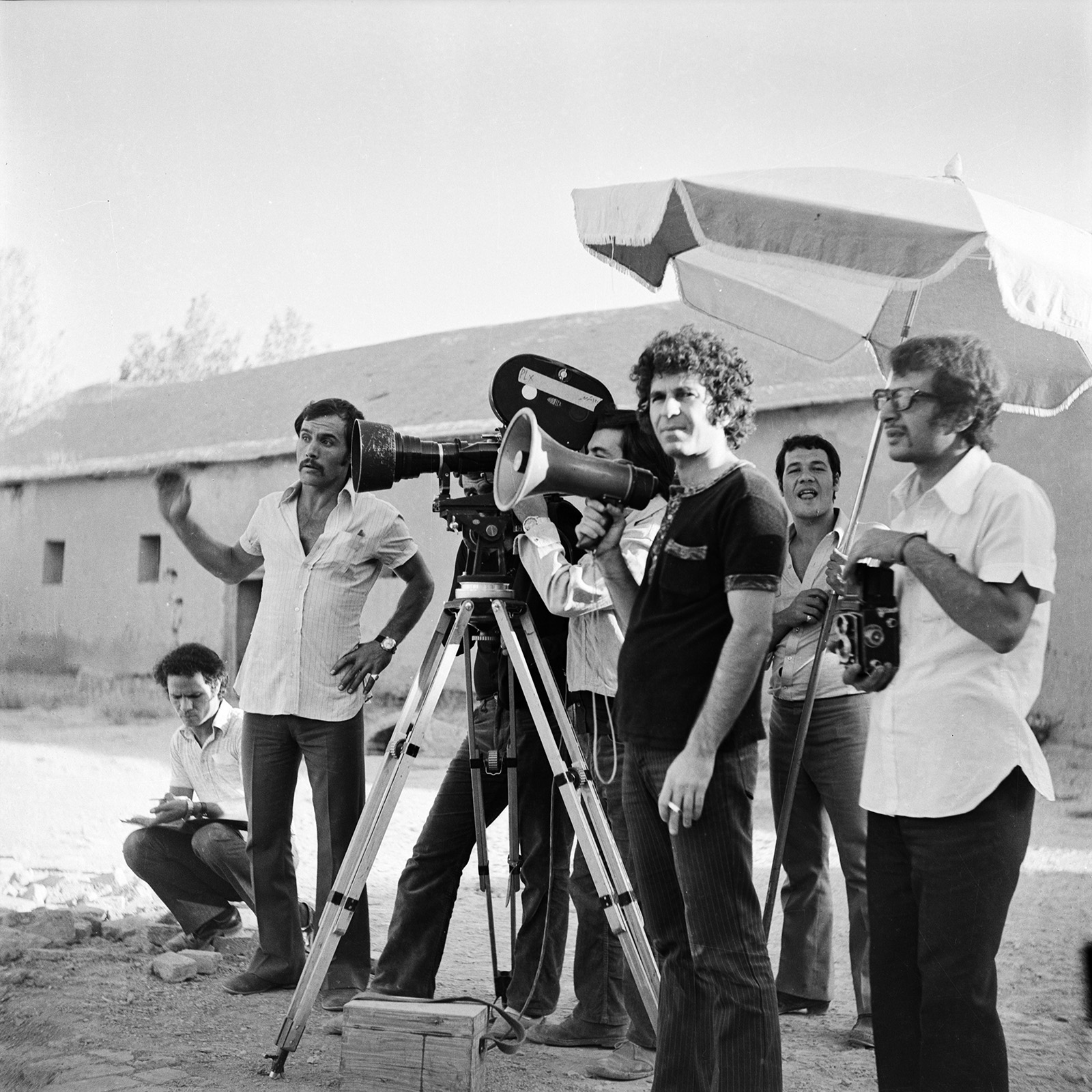 TEHRAN, IRAN - 1972: Dariush Mehrjui (holding a megaphone), the director, seen during the set of "The Postman", in 1972 in Tehran, Iran. Photograph in black and white shows a group of men on a film set.