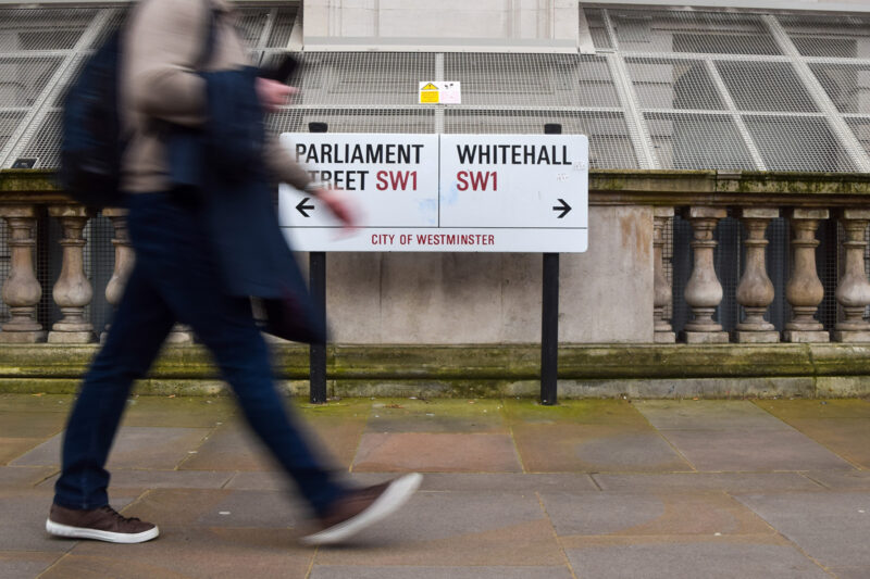 A photograph of a man walking in front of street signs for Parliament Street and Whitehall in Westminster