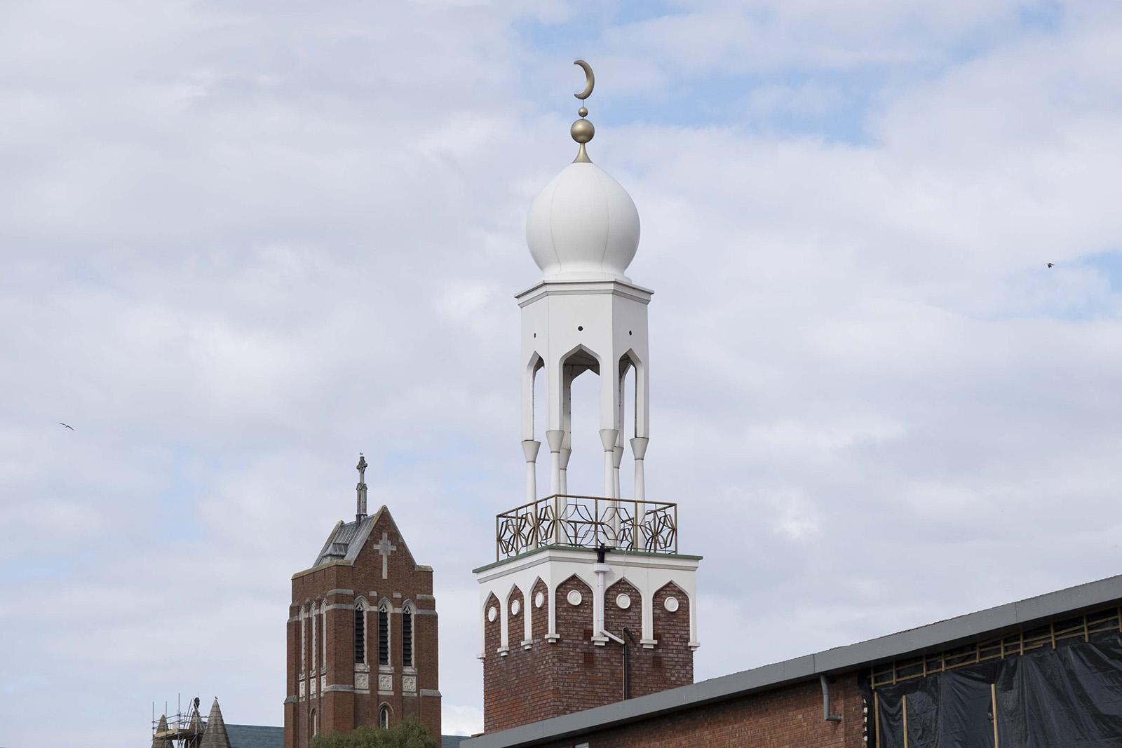 A photograph with the minaret of Birmingham Central Mosque in the foreground, in front of the bell tower of St Alban the Martyr, a Grade II listed Church of England parish church