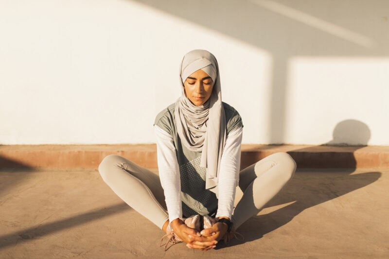 A stock photograph of a woman seated on the floor, doing stretching exercises