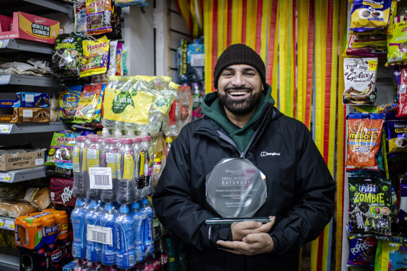 A picture of a smiling Sheraz Awan, owner of the Westerhope Convenience Store, inside the shop holding his Community Champion award