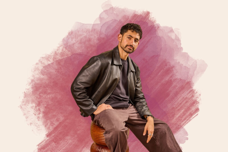 A photograph of actor Amir El-Masry seated, wearing a leather jacket