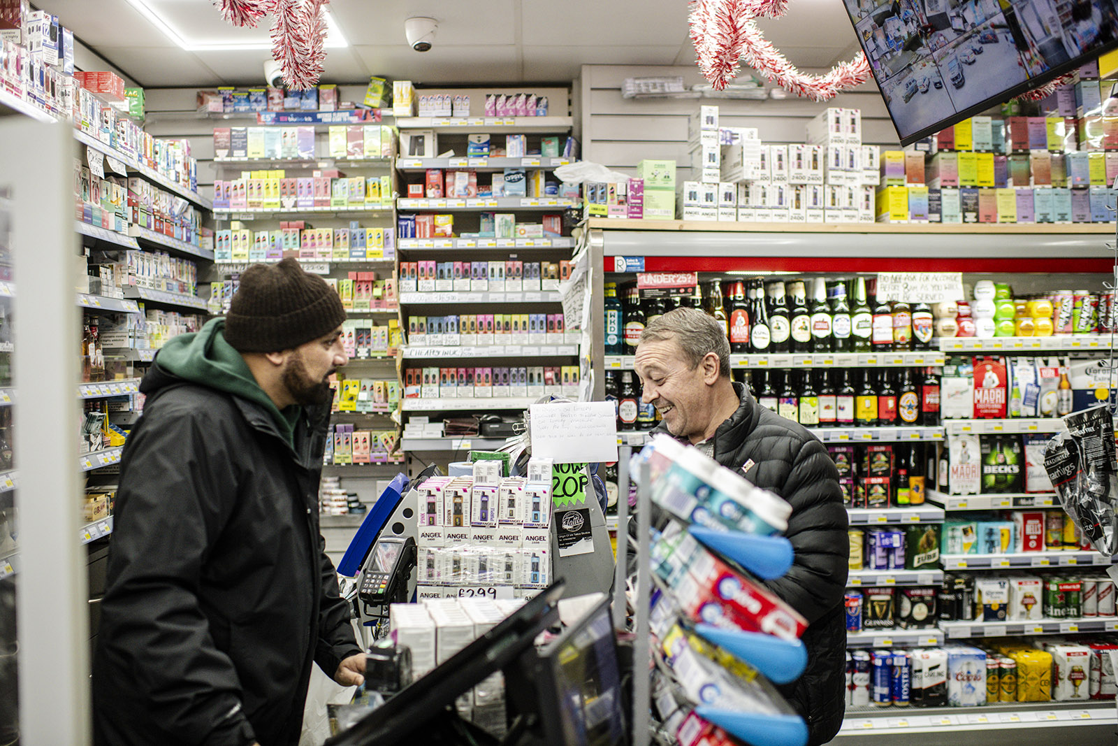 A photograph of Sheraz Awan behind the counter of his shop, talking to a customer