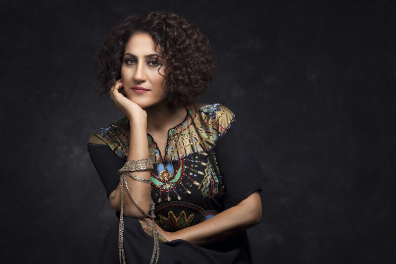 A portrait image of Kurdish singer Aynur Doğan, pictured sitting down with her chin resting on her right palm
