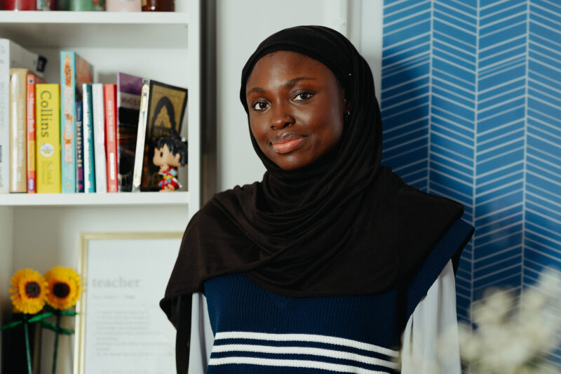 A portrait photograph of Minority Teachers Ireland founder Baisat Alawiye at home, with a bookcase behind her