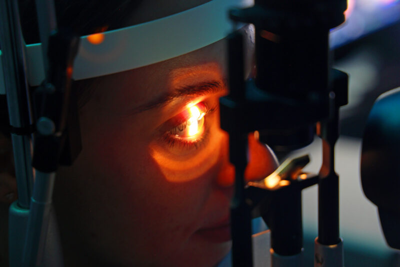 A close-up of a person's eye during an eye test. Red light is being shone onto the eyeball as they look straight ahead