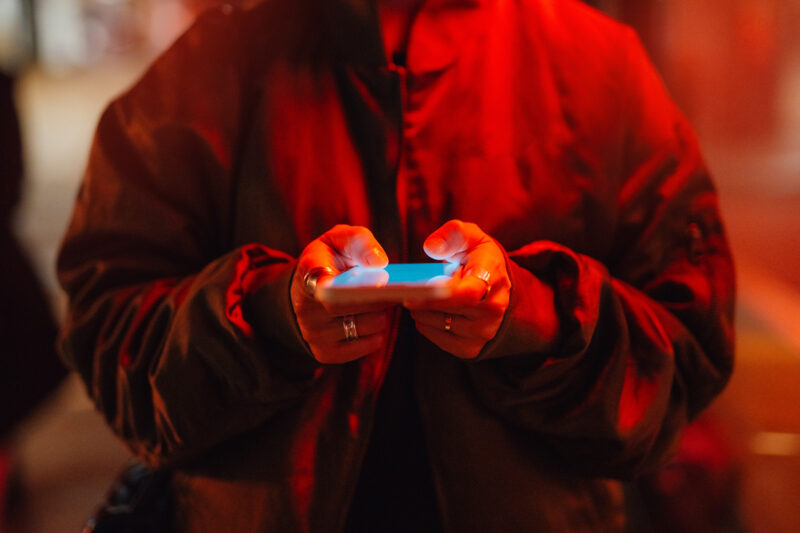 Red lighting on a woman looking at her phone. Her head is not visible
