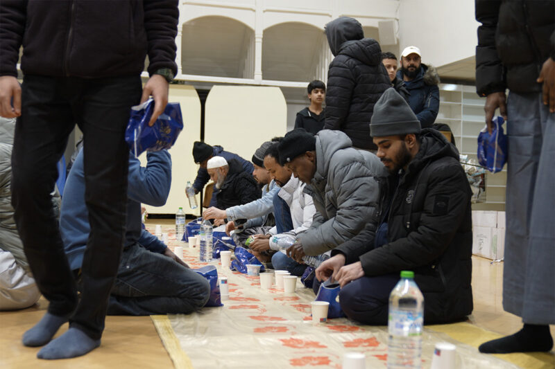 A photograph showing worshippers kneeling down having iftar at Green Lane Masjid, Birmingham