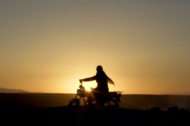 A still from Sara Khaki and Mohammadreza Eyni's Cutting Through Rocks, nominated for best documentary feature at the 2026 Oscars. The image shows a woman on a motorbike, silhouetted against a low sun.