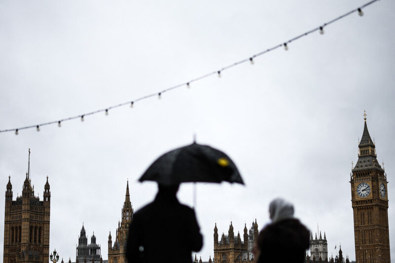 silhouettes of people under umbrellas with the Houses of Parliament in the background