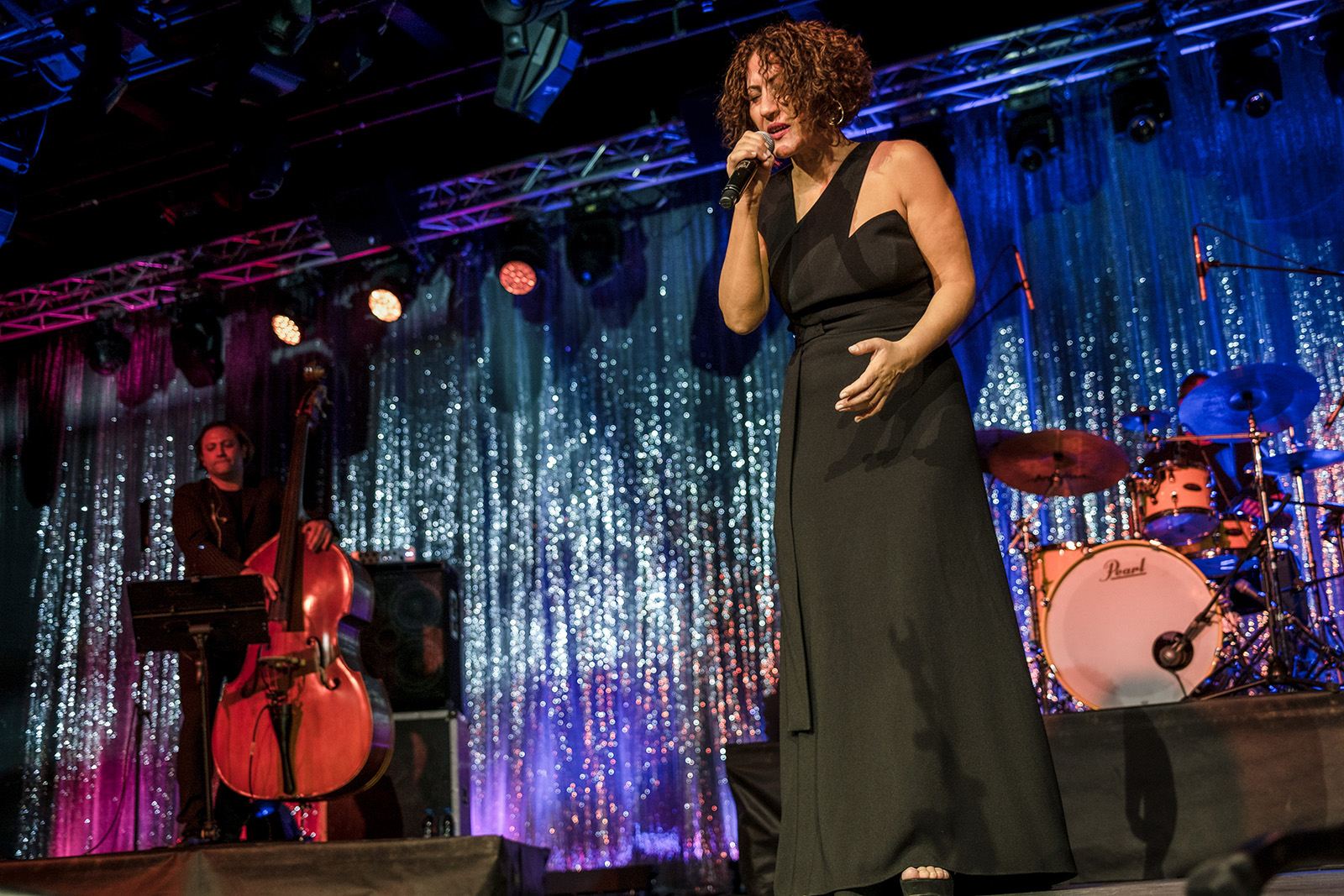 An image of Aynur Doğan performing on stage in a black dress, with a double bass player and drummer behind her, at the Nazim Hikmet Cultural Center in Ankara. 