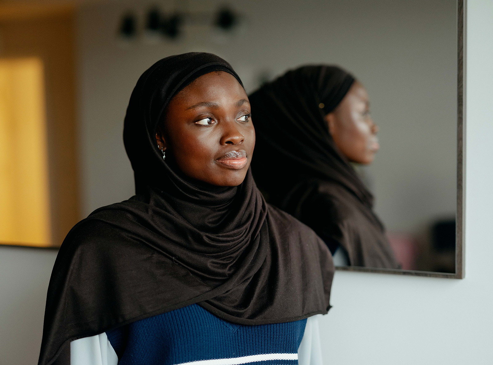 A portrait photograph of Minority Teachers Ireland founder Baisat Alawiye at home, standing in front of a mirror in her living room