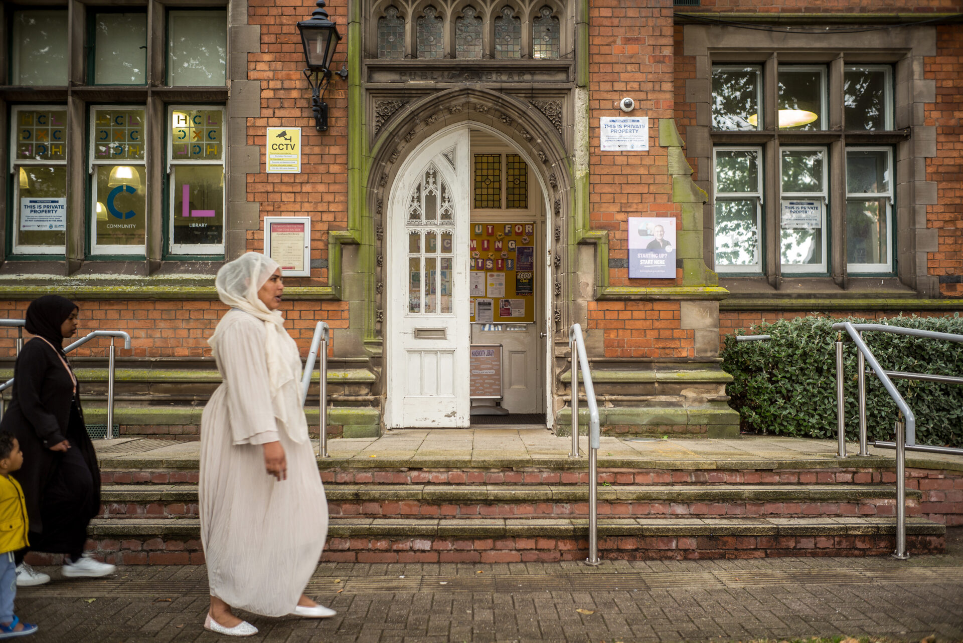 A photograph of a woman and children walking past Handsworth library in Birmingham, where the city council's bankruptcy has put libraries at risk of closure