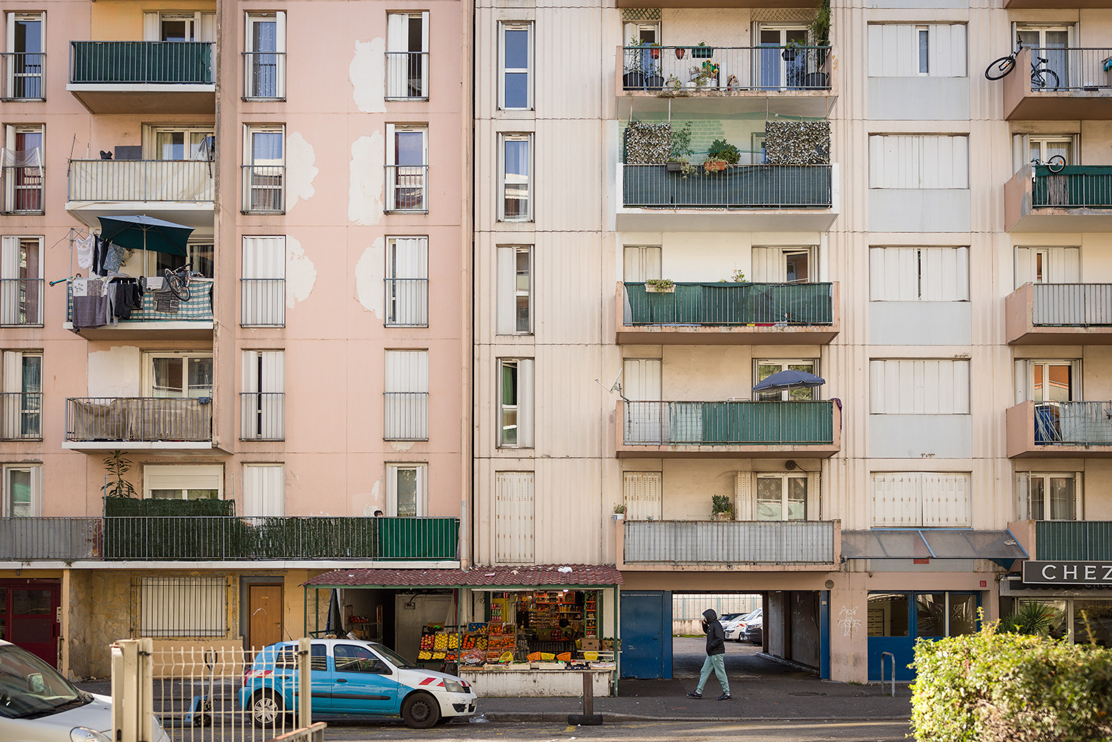 A photograph of a street scene on Rue Guiglionda de Sainte-Agathe, in the L'Ariane district of Nice. One person is walking along the street, near a fruit and veg shop on the ground floor of a residential block of flats