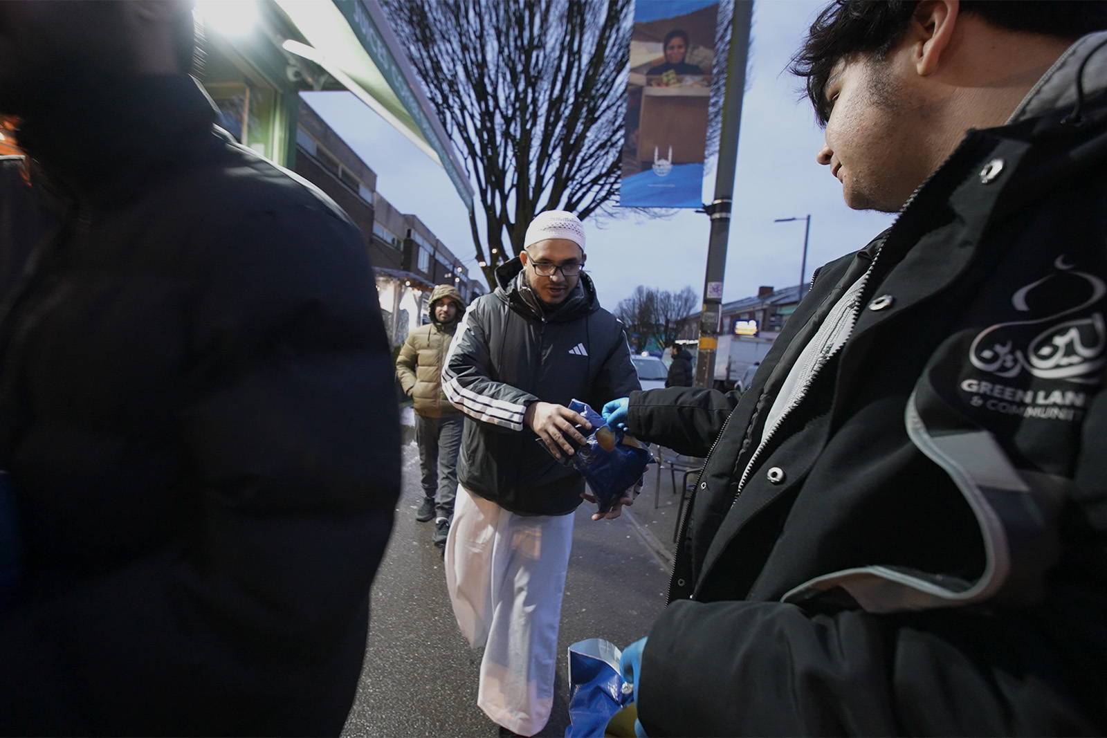 A photograph of a member of the Green Lane Masjid distributing iftar packs on the street in Birmingham