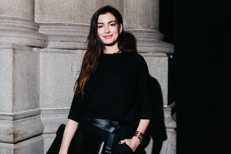 A photograph of Anne Hathaway, wearing an all black outfit and smiling for the camera, at the God’s Love We Deliver Golden Heart Awards in New York, October 2025