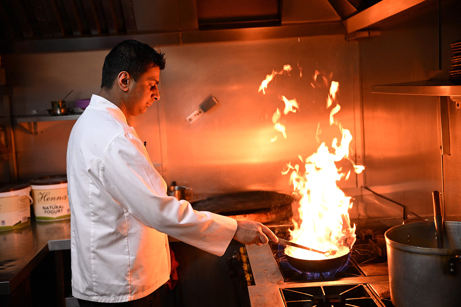 A photograph of head chef Zaf Hussain at work in the kitchen of his restaurant Shababs, with flames leaping around a balti wok on a hob