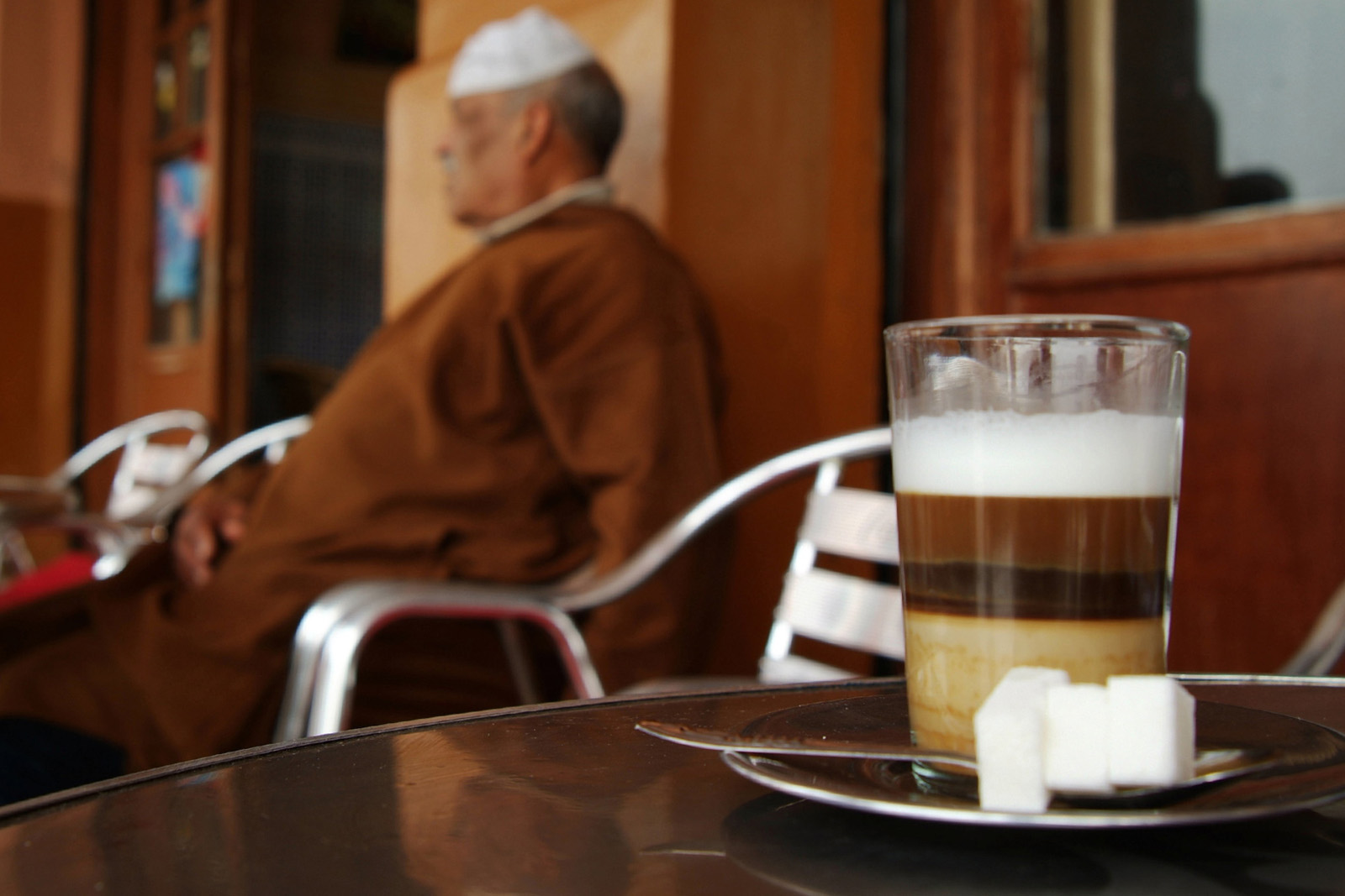 A close-up image of a glass of qahwa nus-nus, served with lumps of sugar and a teaspoon on a saucer, in a Marrakech cafe
