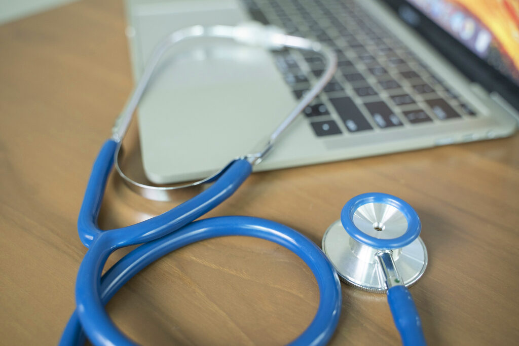 A stethoscope on a desk next to a laptop computer.