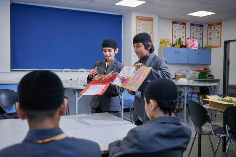 A photograph of students presenting their work in front of a at Madani Boys School