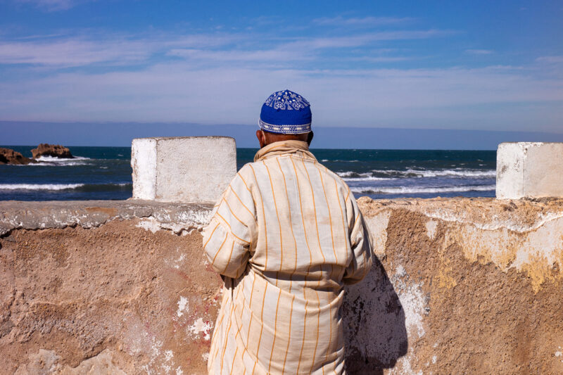 An image of a man looking out to sea, taken from behind. From the series Suzanne, Long Road by Mayssa Jaoudat, part of her wider photographic project Mille-Feuilles