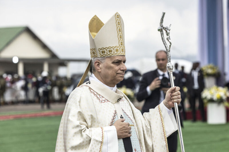 The pope dressed in his mitre (tall hat) and white robe with a staff
