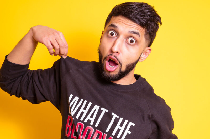 A photograph of Smash Bengali, the stage name of Hashu Mohammed, wearing a slogan sweatshirt and pulling a funny face
