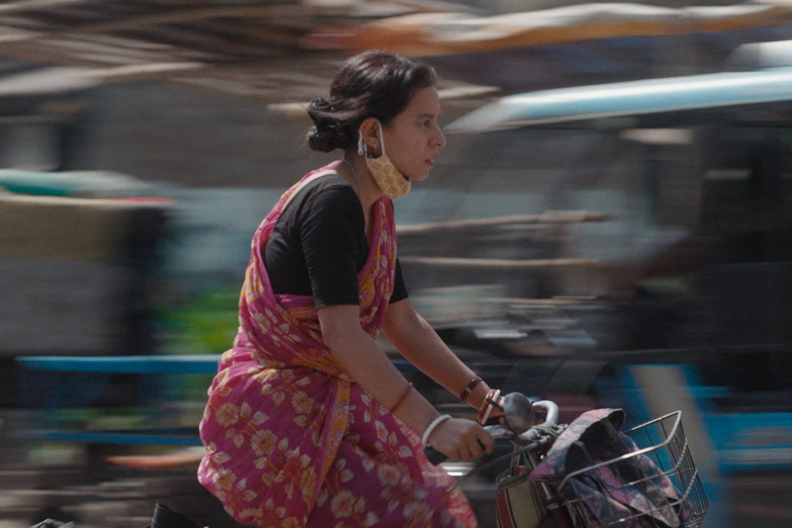 A still image of Tillotama Shome as Maya, the main protagonist in the film Shadowbox, pictured riding a bike on what looks like a busy road